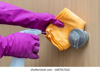 Woman's Hands In Pink Gloves Disinfecting The Doorknob Of The Wooden Door With Spray And Yellow Microfiber Cloth