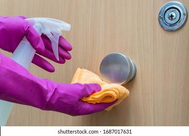 Woman's Hands In Pink Gloves Disinfecting The Doorknob Of The Wooden Door With Spray And Yellow Microfiber Cloth