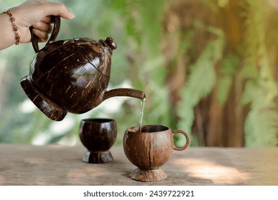 Woman's hands pour tea into a cup made from coconut shells, natural background - Powered by Shutterstock