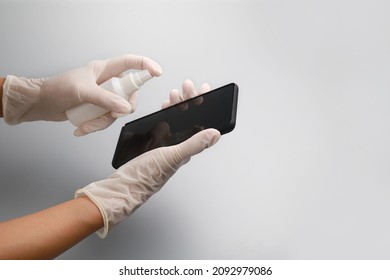 Woman's hands with rubber gloves clean and disinfects a smartphone against a grey background, using disinfection spray to prevent Coronavirus. - Powered by Shutterstock