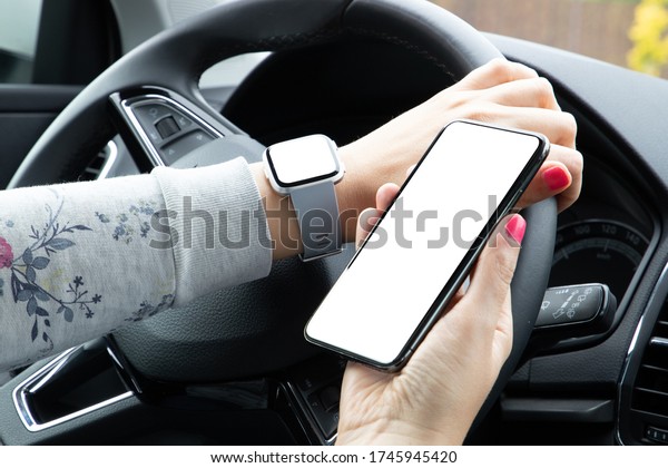 Woman\'s hands with the smart watch \
holding the phone with blank screen in the car\
interior