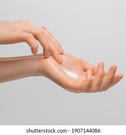 A Woman's Hands Smearing Cream On The Palm Of Her Hand Toward The Brush. Groomed Hands, Natural Short Nails, On A Light Background.