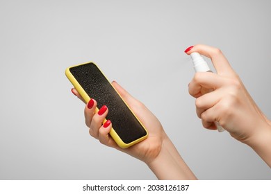 Woman's Hands Spray Disinfectant On Mobile Phone To Clean And Protect Against Viruses. Cleaning Smartphone By Alcohol Hand Sanitizer.