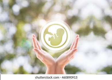 The woman's hands support the human embryo icon on blurred background tree.