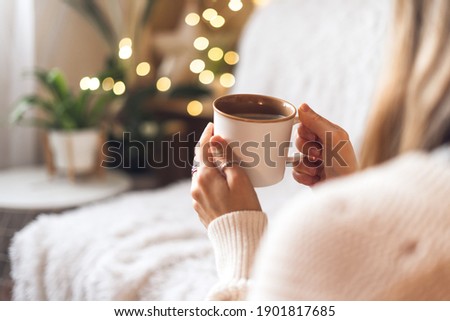 Woman's hands in sweater holding cup of hot drink coffee indoors. Still life composition.