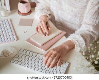 A woman's hands taking notes while using a computer at her desk, a feminine home office scene