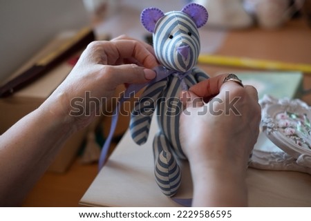 A woman's hands tie a bow around the neck of a sewn bear.