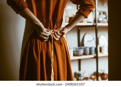 Woman's hands tying an apron, rear view. A potter prepares for work by putting on an apron in the workshop Back view - Powered by Shutterstock