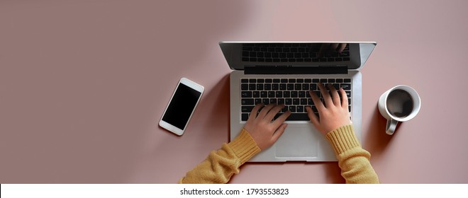 Woman's hands are using a computer laptop at the working table surrounded by a coffee cup and mobile phone.