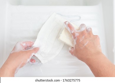 Woman's Hands Washing A Reusable Cloth Face Mask With A Bar Of Soap In A White Porcelain Sink
 
