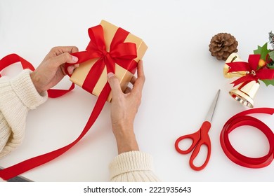 Woman's hands wrapping christmas gift or other holiday handmade present in gold paper with red ribbon. Making bow at present box, decoration of gift, top view. - Powered by Shutterstock