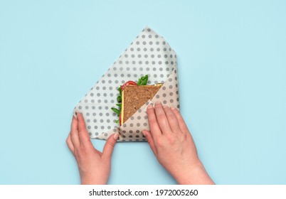 Woman's hands wrapping a sandwich in a beeswax cloth on a blue table, above view. Healthy sandwich with wholemeal bread and vegan ingredients, wrapped in reusable beeswax paper. - Powered by Shutterstock