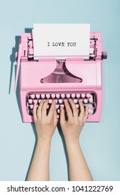 Woman's hands writing "I love you" on an oldschool pink typewriter. Valentine's day.