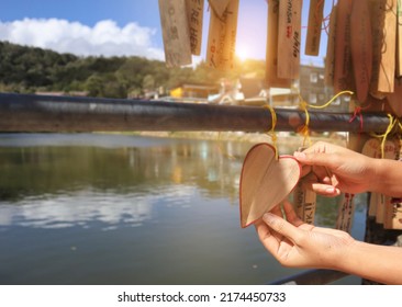 A Woman's Hand-tied A Brown Wooden Name Tag With A Red Border With A Small Heart. On The Iron Pillar In The Background, The View Of The Village And The Light That Shines In The Morning Light. - Image