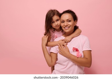 Woman's health , medical concept. Serene woman and girl in pink attire with Breast Cancer Awareness ribbon, daughter hugging her mom, holding by hands, looking at camera, supporting cancer patients. - Shutterstock ID 2039046026