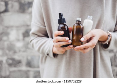 Woman's holding botles with spa cosmetics against gray wall. Beauty blogger, salon therapy, minimalism concept, copyspace