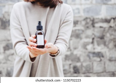 Woman's holding brown glass bottle with spa cosmetics against gray wall.  Beauty blogging, salon therapy, product package, mockup, minimalism concept