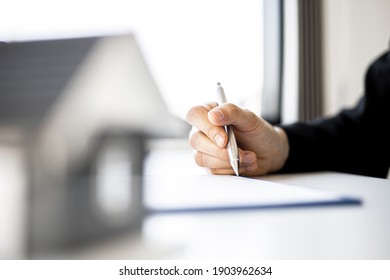 A Woman's Home Salesperson Is Checking Documents For A House Purchase Contract Before Letting The Customer Sign A Contract, On The Table Is A Gray Miniature House Model, Real Estate Trading Ideas. 