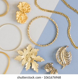 Woman's Jewelry. Vintage jewelry background. Beautiful gold tone brooches, braceletes, necklaces and earrings on blue background. Flat lay, top view