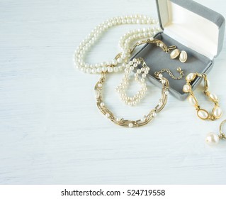 Woman's Jewelry. Vintage Jewelry Background. Beautiful Gold And Pearl Necklaces, Bracelets And Earrings In A Gift Box On White Wood. Flat Lay, Top View