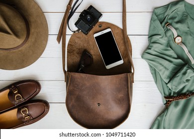 Woman's journalist or traveler accessories on white wooden table background flat lay. Brown leather purse, marine shoes, mobile cellphone, belt, watch, retro film camera. Empty space for copy, text.