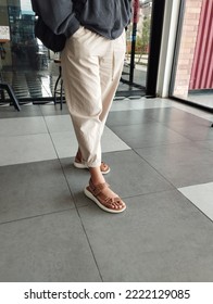 Woman's Leg Wearing Khaki Lounge Pants And Brown Leather Sandals. Eye Level Angle. Selective Focus. Women Fashion And Lifestyle Concept.