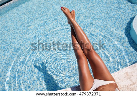 Woman's legs at the blue pool on sunny day 