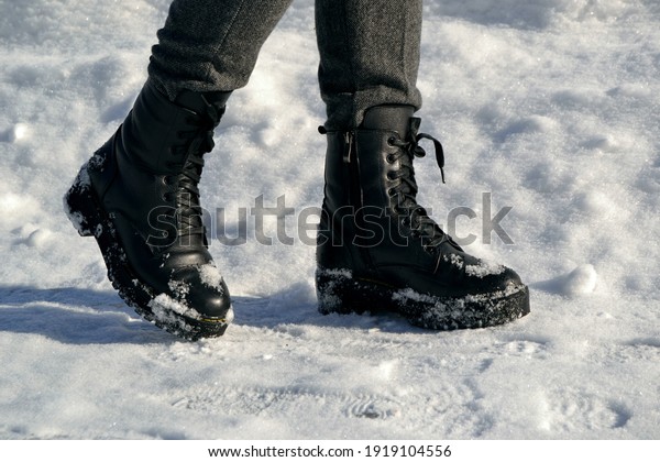 Woman\'s legs in high black boots walking down the\
street in the snow
