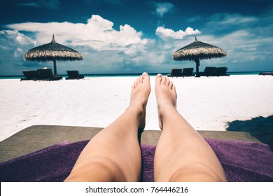 Woman's Legs Laying On A Sunbed, A View Of A Beach And Few Resting Spots. First Person View. Maldives Vacation