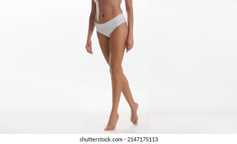 Woman's Legs. Medium Long Shot Of Slim African American Woman In White Underwear Standing On Tiptoes Against White Background | Smooth Legs And Leg Care Concept