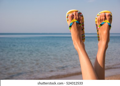 Woman's Legs And Sea. Feet Wearing Flip Flops. 