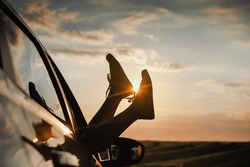 Woman's Legs In Sneakers In The Car Window. Modern Hipster Girl Resting In A Car At Sunset. Summer Travel, Freedom, Happiness Concept