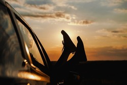 Woman's Legs In Sneakers In The Car Window. Modern Hipster Girl Resting In A Car At Sunset. Summer Travel, Freedom, Happiness Concept