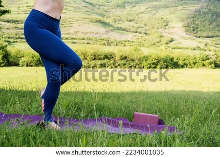 Woman's legs in sporty outfit exercising yoga and stretching on mat in meadow outdoors. Hills landscape on background. Healthy active lifestyle in summer