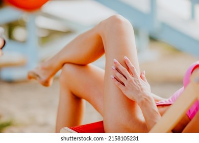 Woman's long slim legs in pink bikini sitting at the chair on the sand beach while sunset. 