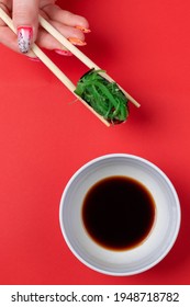 A Woman's Manicured Hands Hold Wooden Sticks Of Green Chukka Roll On A Red Background. Space For Text, Flatlay