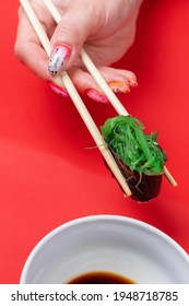 A Woman's Manicured Hands Hold Wooden Sticks Of Green Chukka Roll On A Red Background. Space For Text, Flatlay