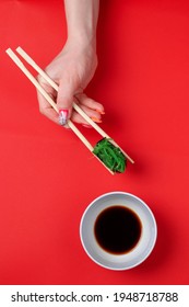 A Woman's Manicured Hands Hold Wooden Sticks Of Green Chukka Roll On A Red Background. Space For Text, Flatlay