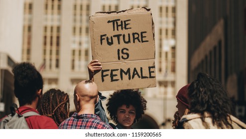 Woman's march protest sign that reads the future is female. Female walking on the city street holding a banner with group of people.