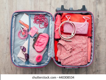Woman's open bag on a desktop with clothing and accessories, she is packing and getting ready to leave, travel and vacations concept