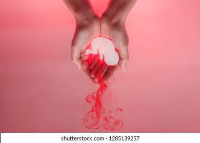 Womans palms pressed together and keep embryo. from paper .Red lood comes from the baby and looks like abortation. Hands are located at the top. Pink background.