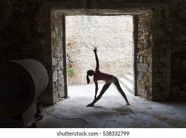 Womans silhouette in Trikonasana yoga pose inside of old building