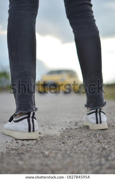 woman\'s standing with a blurry yellow car\
background, in the middle of her leg or\
foot