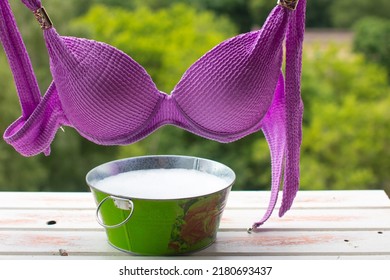 A Woman's Swimsuit Dries On A Rope. Metal Basin With Soapy Water