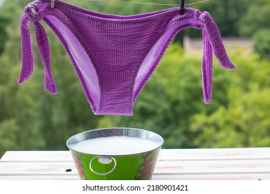 A Woman's Swimsuit Dries On A Rope. Metal Basin With Soapy Water