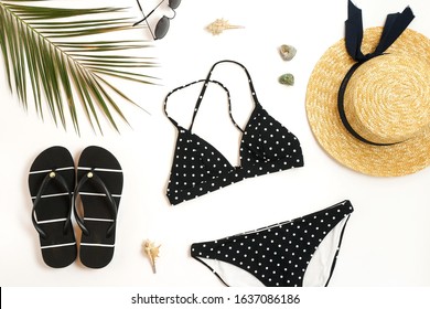 Woman's swimwear and beach accessories flat lay top view on white background. black and white polka dot bikini swimsuit, straw hat, shoes, sunglasses, palm leaf, sheels. Copy space