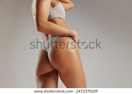 Woman's toned back and buttocks in light gray ribbed underwear against grey studio background. Model with athletic figure. Concept of beauty and fashion, female health, anti-cellulite, dieting. Ad