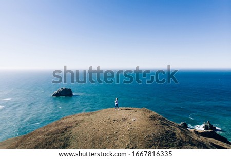 Woman's traveler silhouette standing on bank of sea at high cliff looking at water surface and scenic environment, female tourist enjoying scenery of ocean during journey on wild nature in summer