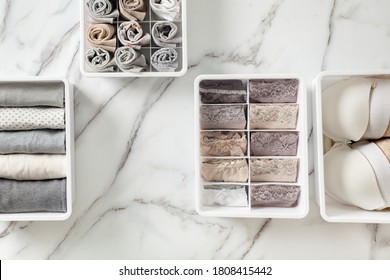 Womans underwear, pajamas and socks neatly folded and placed in closet organizer drawer divider on white marble table. Declutter wardrobe of undergarments. Keeping organized lingerie drawer storage.