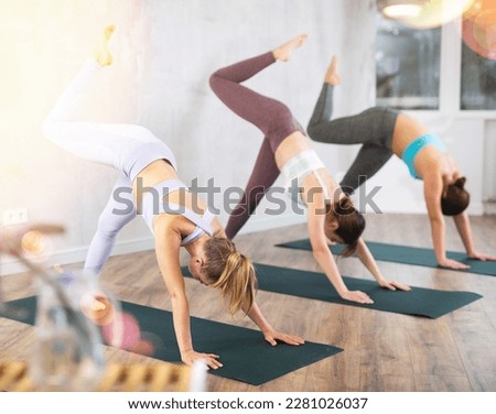 Women in activewear performing basic pose Downward Facing Dog Adho Mukha Svanasana for flexible shoulders and healthy back during yoga class in studio